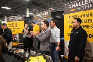 six people standing behind a challenger homes booth at a convention.