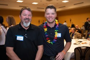 Two men posing for a photo at an event, one wearing a lei