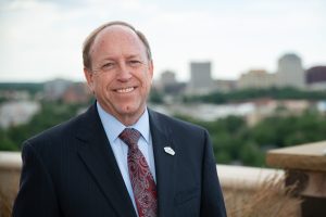 individual photo of John Suthers with downtown Colorado springs in the background